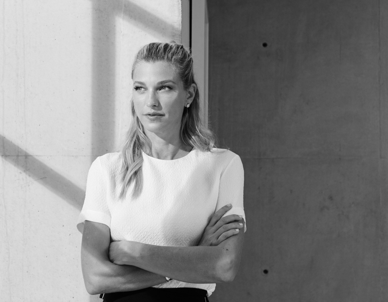 Nicole Junkerman steht mit verschränkten Armen vor einer schlichten Betonwand.